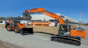 Hitachi team holding a Thank You banner behind an excavator and wheel loader